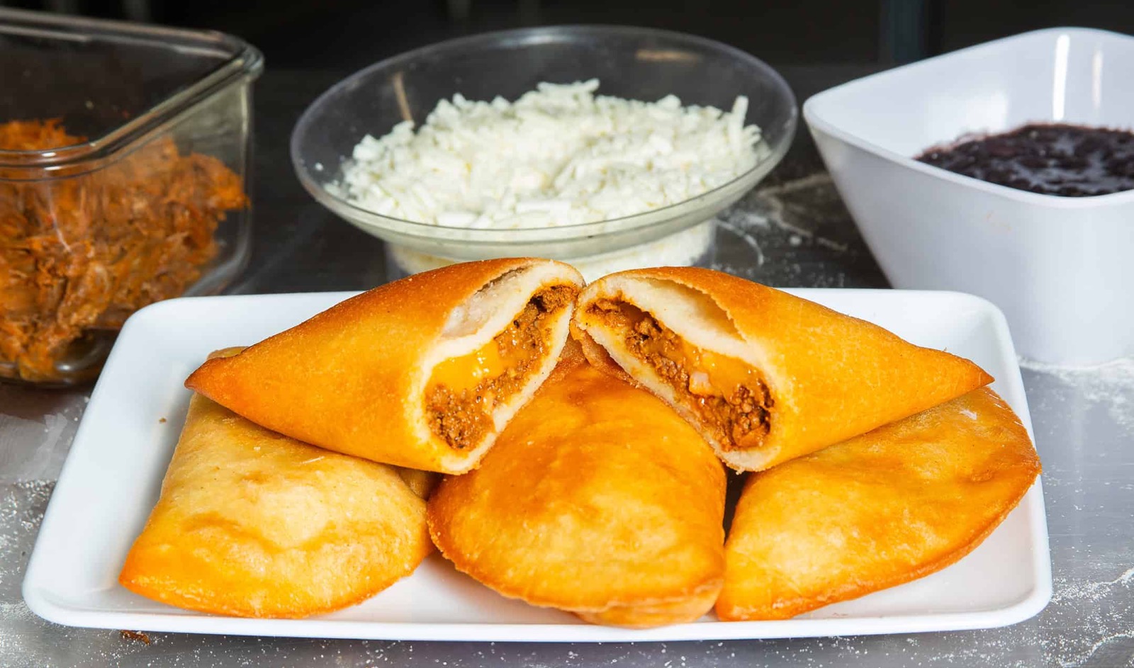 A halved empanada showing a hot beef and melted cheese filling, with queso blanco and black beans behind it.