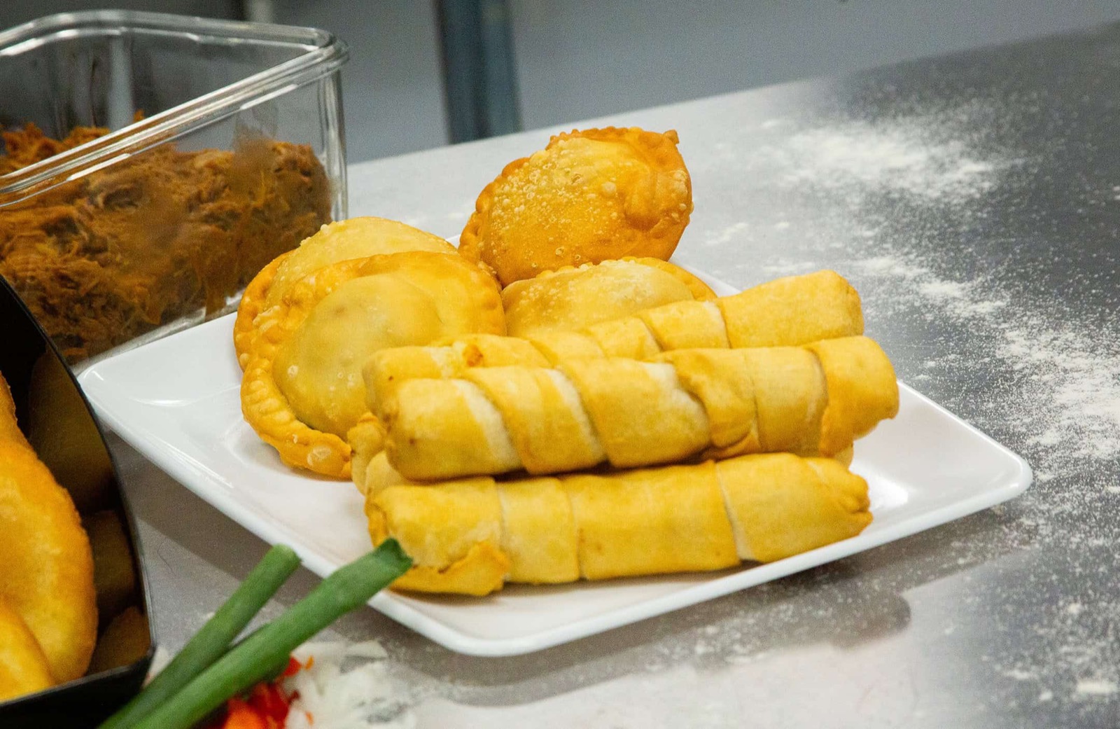 Golden empanadas and rolled tequeños plated beside a tray of seasoned shredded beef.