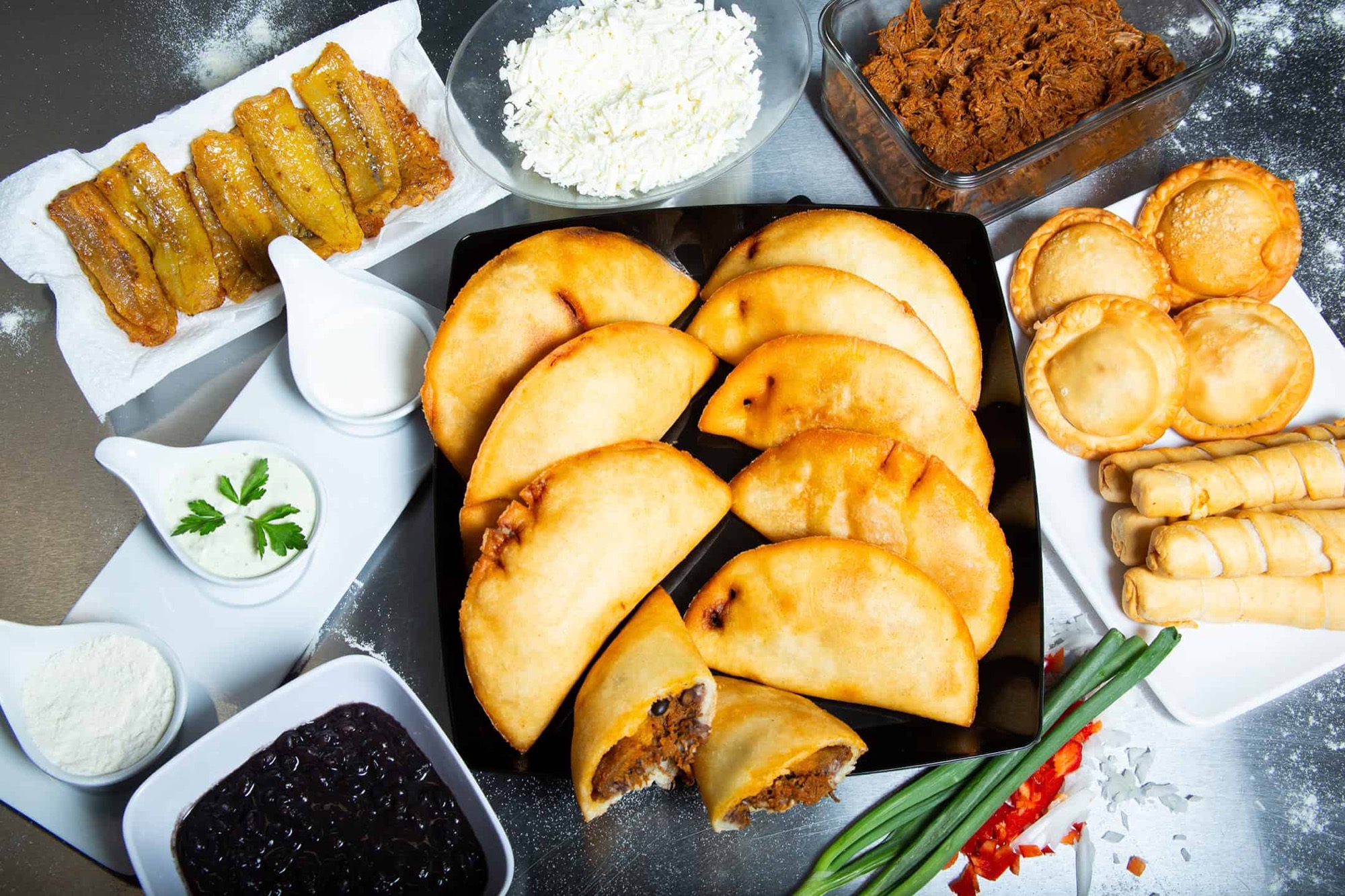 A full spread of Venezuelan empanadas, tequeños, sweet plantains, queso blanco and shredded beef on a prep table.