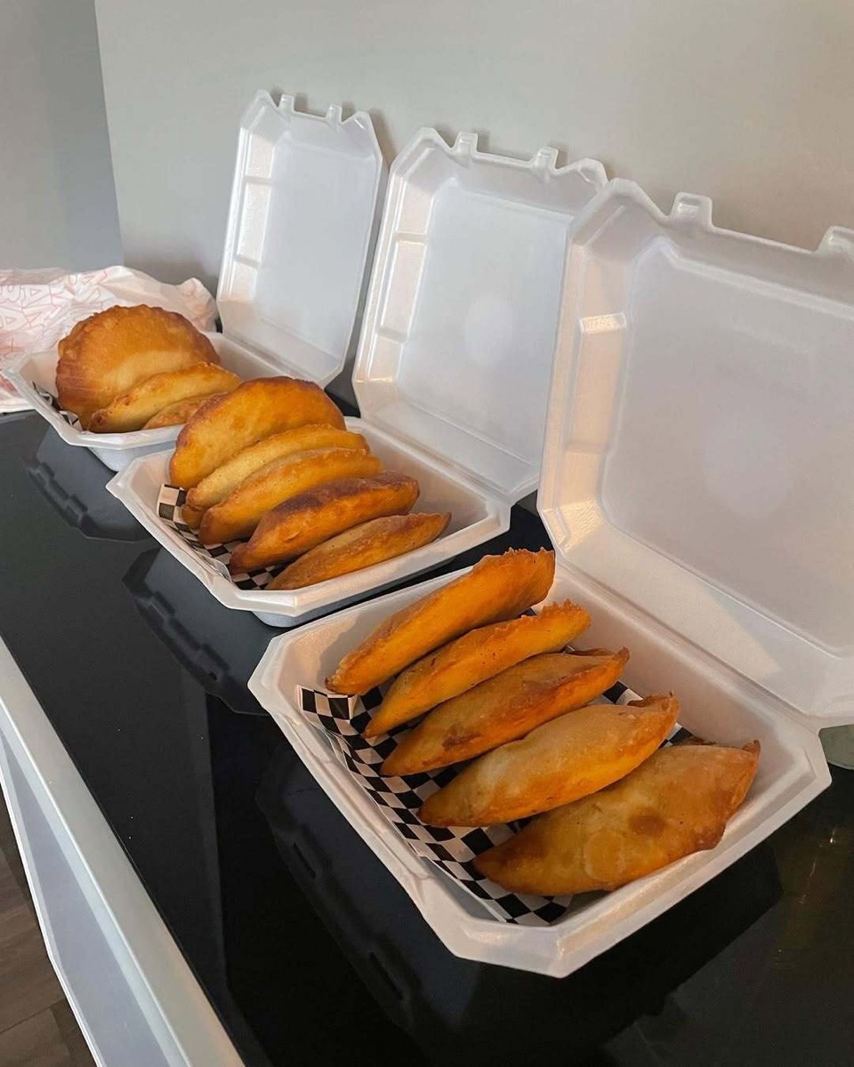 Takeout containers packed with golden Venezuelan empanadas, ready to go.